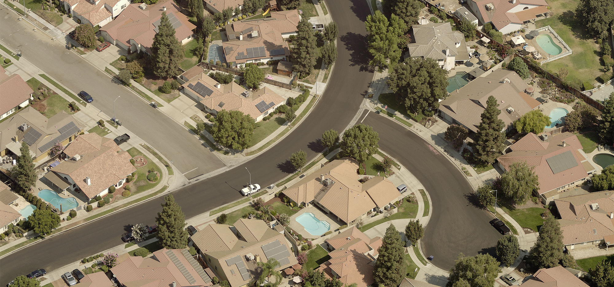 Solar panels on the roofs of several suburban homes in a sunny cul-de-sac.