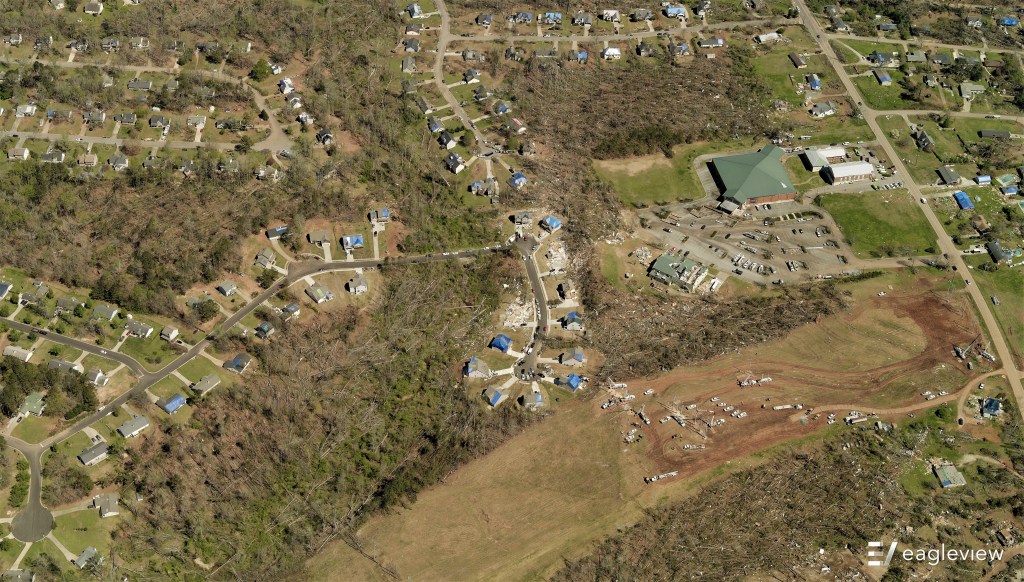 The wide view provides additional context of the tornado's aftermath, from damaged roofs to downed trees.