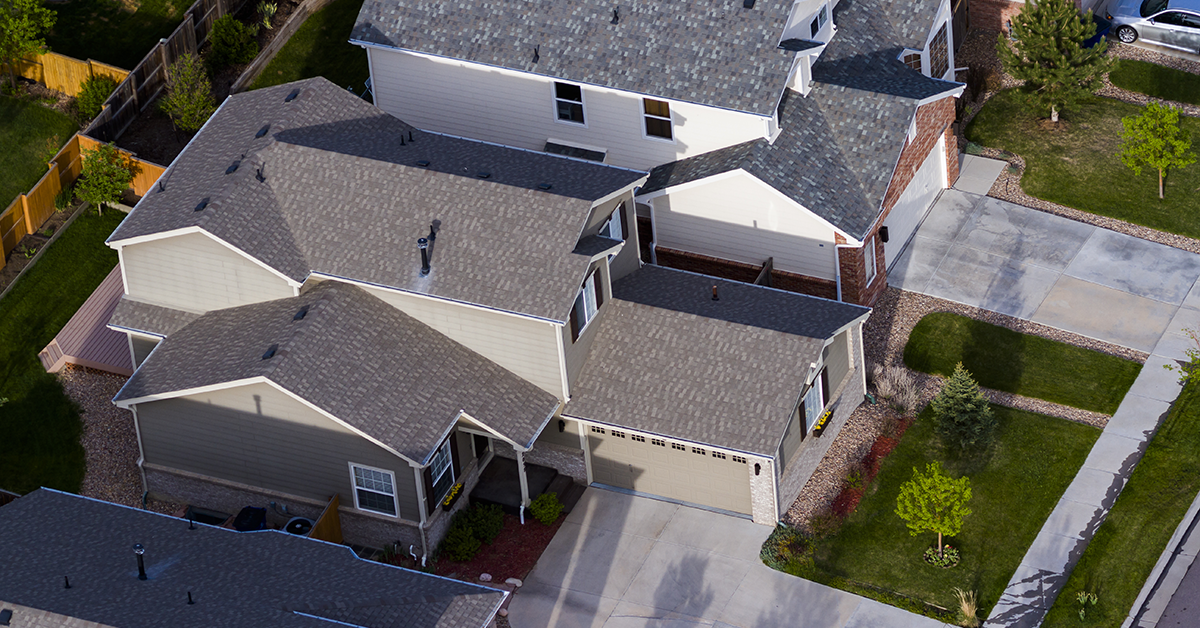 "Aerial view of a suburban neighborhood featuring two-story modern homes with gabled roofs, beige and gray exteriors, and neatly maintained front lawns and driveways. The houses are closely spaced, showcasing a planned residential community layout.