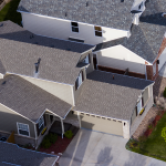 "Aerial view of a suburban neighborhood featuring two-story modern homes with gabled roofs, beige and gray exteriors, and neatly maintained front lawns and driveways. The houses are closely spaced, showcasing a planned residential community layout.