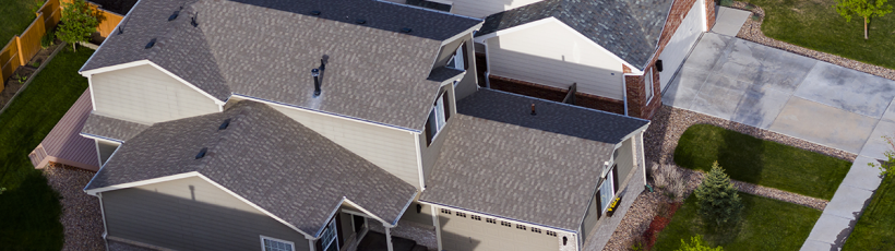 "Aerial view of a suburban neighborhood featuring two-story modern homes with gabled roofs, beige and gray exteriors, and neatly maintained front lawns and driveways. The houses are closely spaced, showcasing a planned residential community layout.