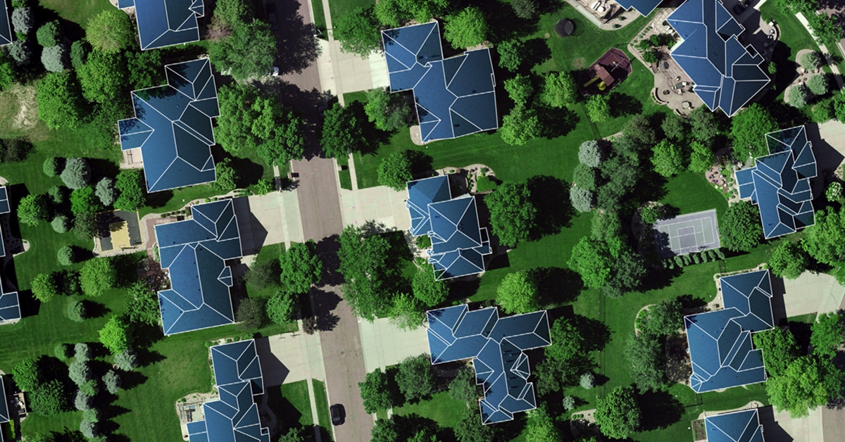 Aerial view of a suburban neighborhood with houses, trees, and lawns, with rooftops outlined in blue.