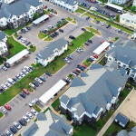 Apartment building aerial view showing multiple residential buildings, parking lots, and green landscaped areas.