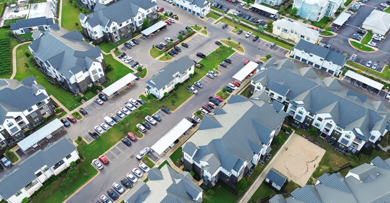 Apartment building aerial view showing multiple residential buildings, parking lots, and green landscaped areas.